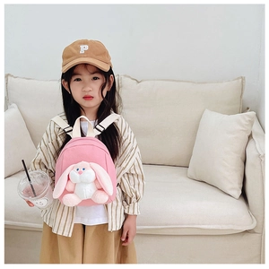 Pink children's backpack with a 3D plush bunny doll shown on a cozy sofa background