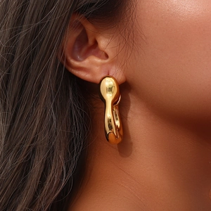 Detail of a large gold hollow earrings showing streamlined irregular shape on model