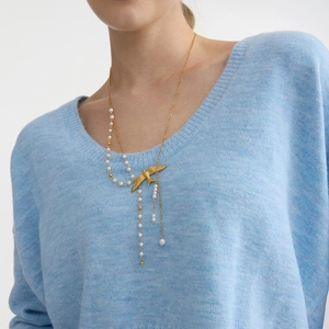 Detalle de un collar de golondrina dorada con perlas sobre un suéter de punto azul