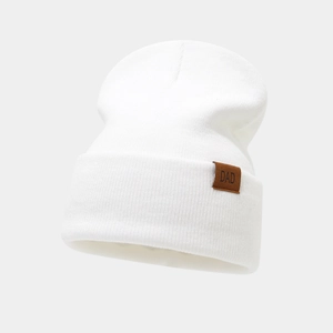 Detailed close-up of white knitted beanie with brown leather DAD patch label and ribbing