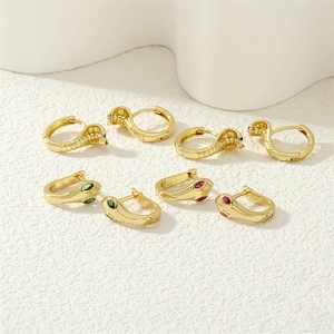 Detail of gold snake earrings featuring green and red crystals on a white surface