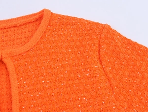 Detailaufnahme von orangefarbenem Strickpullover mit schimmernden Pailletten