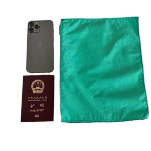 Green lightweight nylon drawstring storage bag shown next to a passport for size