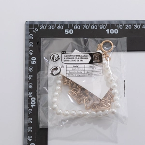 Macro view of gold chain pearl necklace packaging showing scale with ruler reference