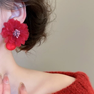 Detail of red fabric flower earrings with crystal tassel worn on a warm red sweater