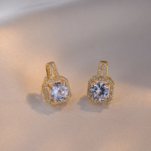Boucles d'oreilles carrées halo dorées avec zircone cubique sur fond de soie