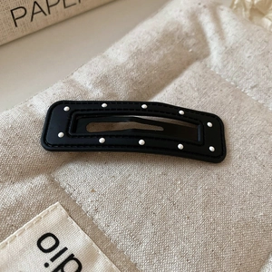 Detail of a matte black hair clip with white polka dots on a beige quilted background