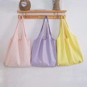 Three minimalist canvas tote bags in pink, purple, and yellow hanging on a wall
