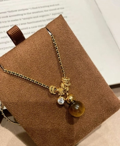 Detail view of tiger eye stone necklace with gold chain on brown display stand