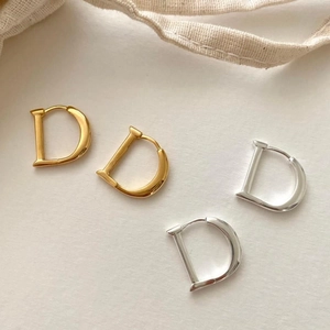 Polished D-shaped gold and silver huggie earrings displayed on a minimalist background