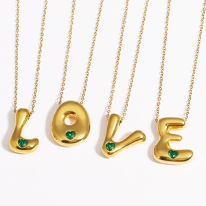 Macro detail of gold-plated LOVE letter pendants featuring inlaid green heart-shaped gems