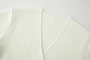 Detail des V-Ausschnitts einer weißen Strickjacke mit feiner Verarbeitung und weicher Textur