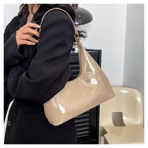 Model wearing a glossy beige patent leather baguette shoulder bag with a sleek finish