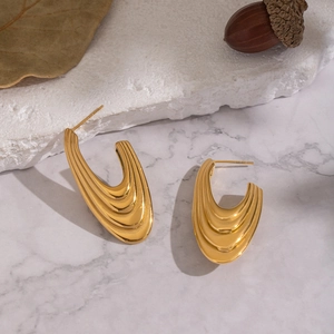Vue détaillée de boucles d'oreilles dorées en U avec texture ondulée sur pierre