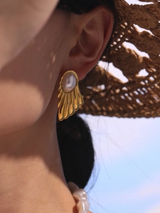 Close-up of gold fan-shaped pearl earrings worn by a model in a summer vacation scene