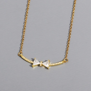 Close-up of golden bow pendant with white zircon stones on a grey textured background
