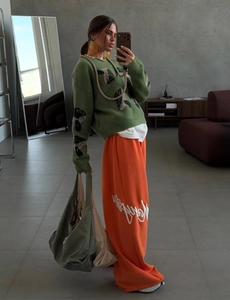 Detail of green mushroom jacquard knit sweater with orange wide-leg trousers