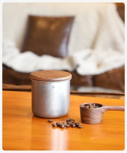 Detailed view of a metal coffee bean storage jar with a wooden lid and a bird emblem
