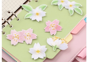 Close-up of pink and white floral embroidery patches on a green notebook cover