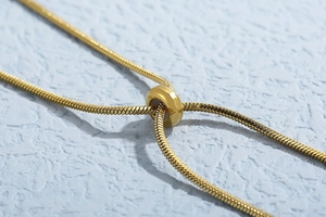 Detail of adjustable gold snake chain necklace with polished sliding bead closure