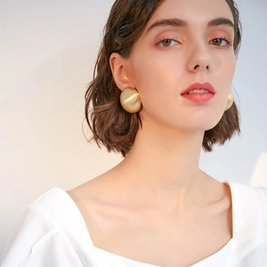 French style gold spherical ball earrings with matte finish worn by model in a soft studio light