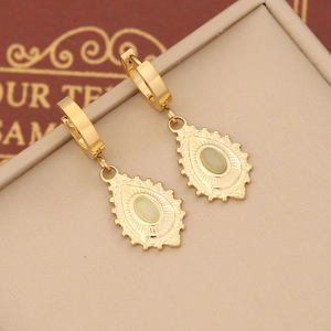 Detail of golden teardrop earrings with inset green gemstones on jewelry display