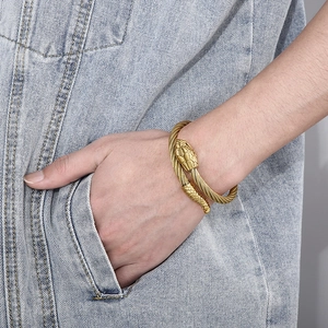 Macro detail of golden snake head bangle featuring twisted wire texture on denim background