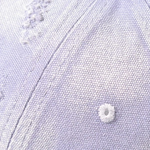 Macro detail of breathable embroidered eyelet and stitching on light purple canvas cap