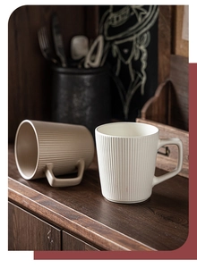 Detail of ceramic mugs with vertical ribbing and square handles on dark wood shelf