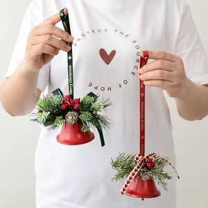 Red Christmas bell ornament with pine needles and cones held by hand for festive decoration