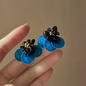 Detail of flower stud earrings featuring black petals and blue iridescent shell layers