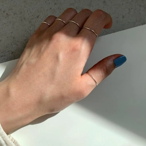 Detail of five minimalist S925 sterling silver rings stacked on fingers in sunlight