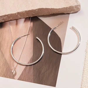 Detailed close-up of polished silver C-shaped hoop earrings on elegant textured stone
