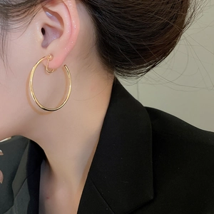 Close-up of model wearing large minimalist golden hoop earrings with polished finish