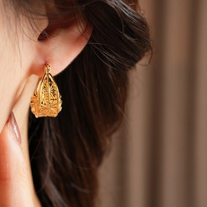 Close-up of golden geometric hollow floral hoop earrings worn by a model
