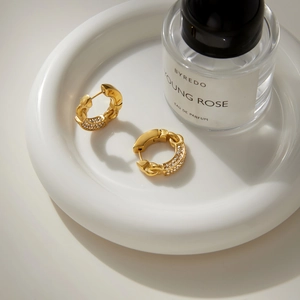 Detail of gold chain-style earrings with zircon pavé on a white ceramic tray