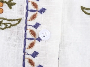 Detail of multi-color floral embroidery and white resin button on cotton linen shirt