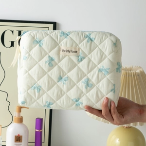 Gros plan d'une trousse matelassée en coton avec nœuds bleus tenue devant un coiffeuse