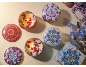 Close-up of scented soy wax candle with dried flower petals in a colorful mandala tin