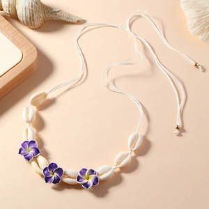 Détail d'un collier de coquillages fait main avec fleurs de frangipanier violettes