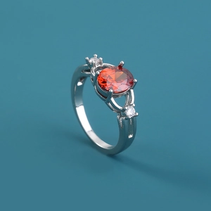 Silver ring with oval red gemstone and white zircon side stones on teal background