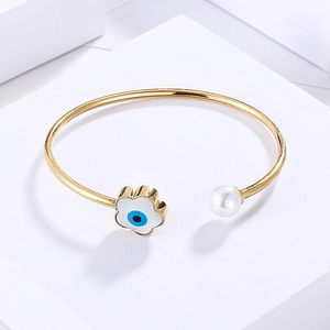 Detail of gold open bangle with white pearl and blue evil eye flower charm ornament