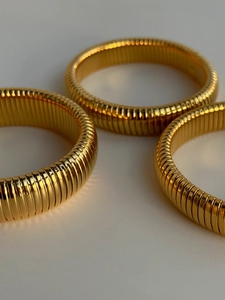 Macro view of three gold polished Tubogas elastic bracelets with fine ribbed texture