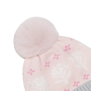 Close-up of pink knit hat featuring white flower jacquard patterns and a large faux fur pompom