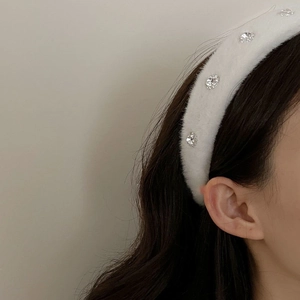 Elegant white plush headband with crystal embellishments worn by a model in soft light