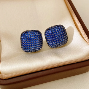 Detailed close-up of vintage square blue zircon studs on white silk padding