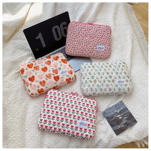 Quilted floral laptop sleeve collection with heart and tulip patterns on a white bed