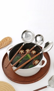 Detail of walnut handle and forged stainless steel ladle in a white ceramic cooking pot