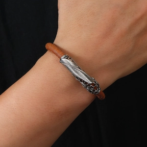 Detail of vintage brown leather bracelet featuring engraved silver feather metal clasp
