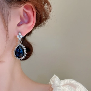 Detail of silver drop earrings with blue crystal and diamonds worn by a model